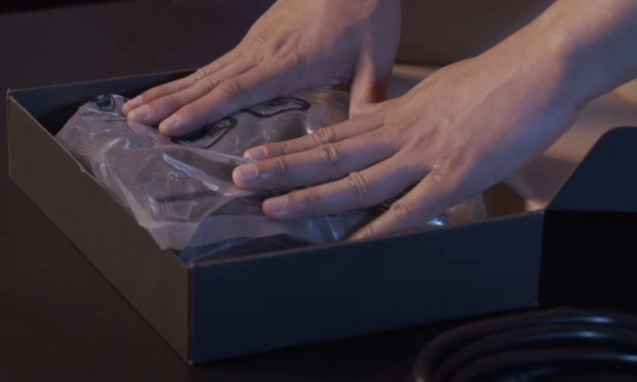 hands touching plastic bags of electronic cords in small brown box